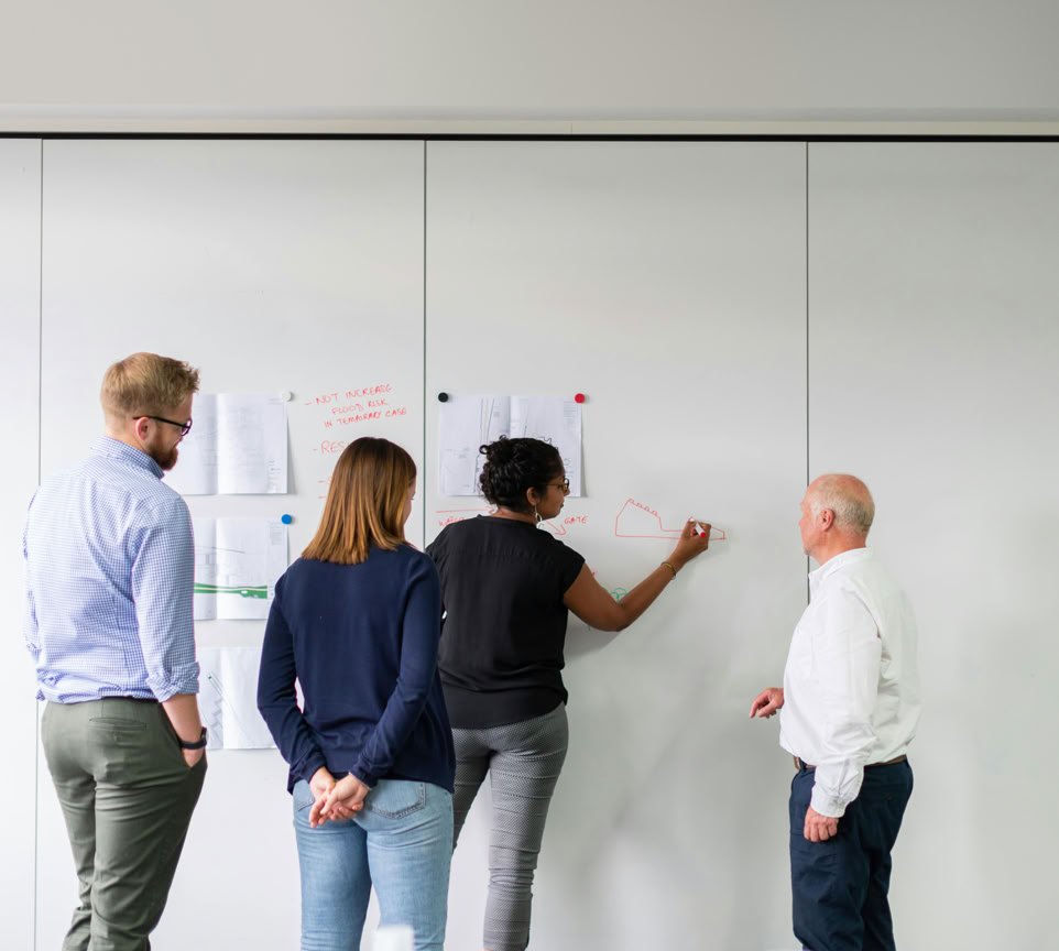 A diverse team of professionals engaged in strategic planning using a whiteboard in an office setting.