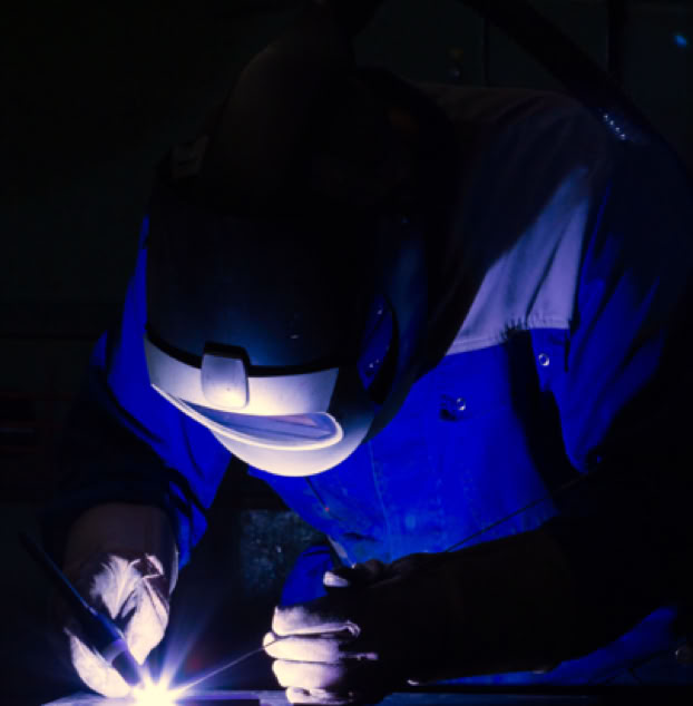 A female worker in a blue uniform smiles while working at a textile factory, surrounded by machinery.
