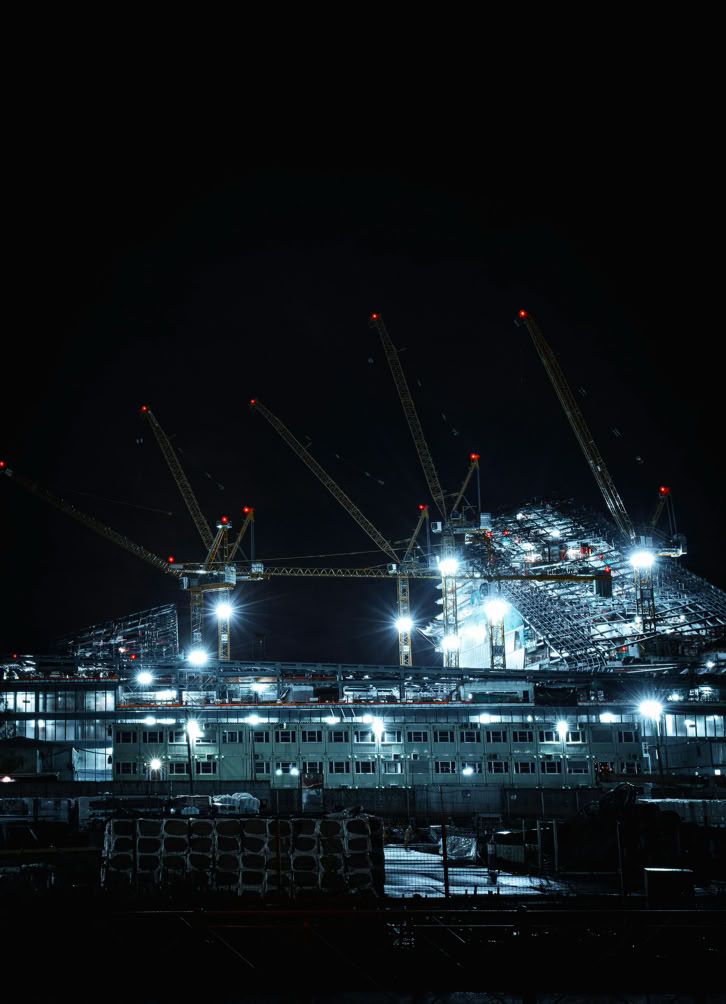 A striking night shot of a large illuminated construction site with multiple cranes.